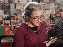 a woman wearing glasses is looking at her phone in front of a wall of comic books including one that says hit