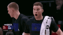 a man with a towel around his neck is standing in front of a scoreboard during a basketball game .