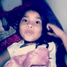 a little girl is laying on a bed with a pink blanket and looking at the camera .