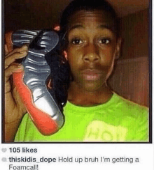 a young boy in a green shirt is holding up a pair of shoes .