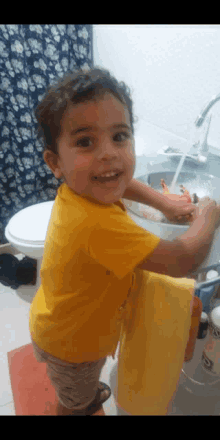 a little boy in a yellow shirt is washing his hands in a bathroom sink