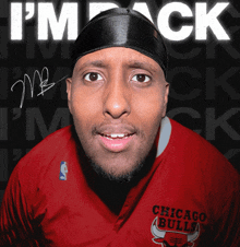 a man wearing a red chicago bulls shirt stands in front of a sign that says i 'm back