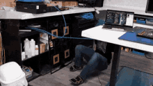 a man is kneeling down under a desk with a laptop on it .