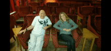 a man and a woman are sitting in red chairs in an empty auditorium