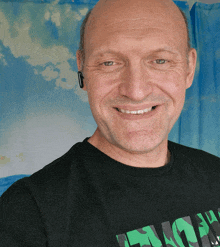 a bald man wearing a black shirt that says " lucky " smiles for the camera