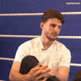 a man in a white shirt is sitting in a boxing ring with his hands folded in front of him