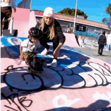 a woman kneeling next to a child on a skateboard with graffiti on the wall that says ' ao '