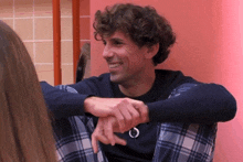 a man with curly hair is sitting in front of a pink wall smiling