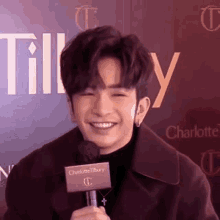 a young man is smiling while holding a microphone in front of a red background .