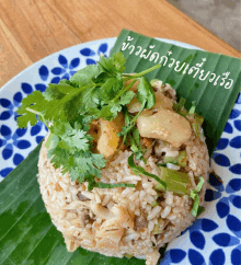 a blue and white plate with rice and vegetables on a banana leaf with thai writing