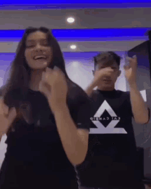 a boy and a girl are dancing together in a room . the girl is wearing a black shirt with a triangle on it