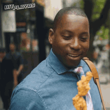 a man in a denim shirt and tie is holding a piece of fried chicken in front of a sign that reads bit playas