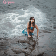 a woman in a mermaid costume is kneeling on a rock in the ocean