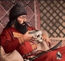 a man with a beard is sitting on a couch holding a skull in his hand .