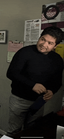 a man in a black sweater is standing in front of a wall with papers on it