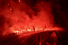 a group of people standing on a bridge with red smoke coming from them