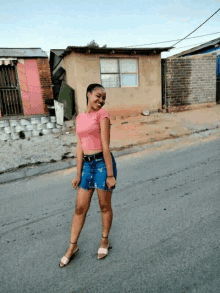 a woman in a pink shirt and blue shorts stands on a street