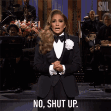 a woman in a tuxedo stands on stage and says no shut up