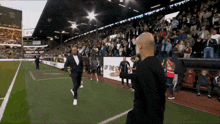 a man in a suit walks on a soccer field in front of a sign that says up the score