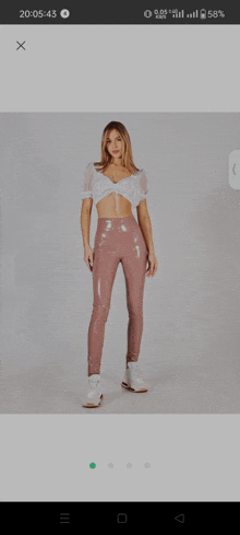 a woman wearing a white crop top and pink pants is displayed on a phone screen