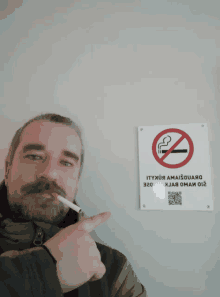 a man smoking a cigarette pointing at a no smoking sign