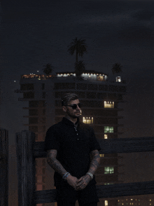 a man in a black shirt and sunglasses stands in front of a building at night