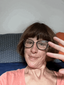 a woman wearing glasses and a pink shirt is making a peace sign