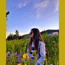 a woman standing in a field of flowers with a blue sky behind her