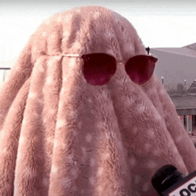 a person wearing sunglasses is covering their face with a pink fur coat