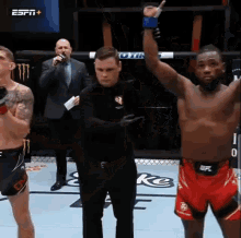 a referee stands between two fighters in a boxing ring while one of them raises his hand in the air