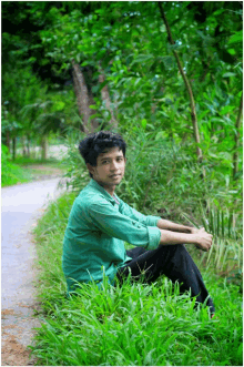 a young boy in a green shirt sits in the grass