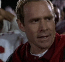 a man in a red shirt is sitting in a stadium watching a game .