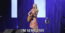 a woman singing into a microphone while holding a guitar and the words " i 'm sensitive " above her