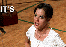 a woman in a white shirt is sitting on a wooden floor with the words it 's on the bottom