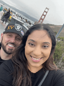 a man and woman are posing for a picture and the woman is wearing a raiders hat