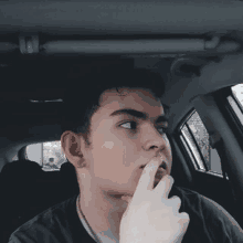 a young man is sitting in the back seat of a car with his finger on his mouth .