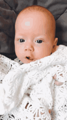 a baby is wrapped in a white blanket and looks at the camera