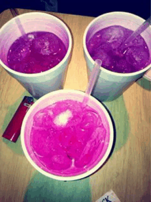 three cups of purple liquid with ice and a straw on a table .