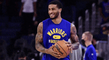 a man wearing a blue warriors jersey holds a wilson basketball