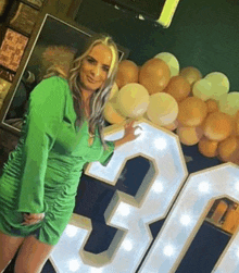 a woman in a green dress is standing in front of a large 30 sign .