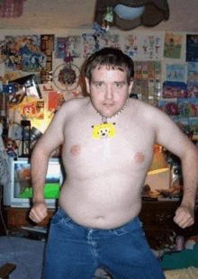 a shirtless man wearing a necklace with a pikachu on it stands in front of a wall that has posters on it