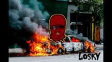 a picture of a burning car with a person wearing a red ski mask .