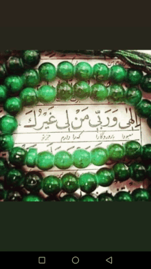 a bunch of green beads are sitting on a piece of paper with arabic writing on it