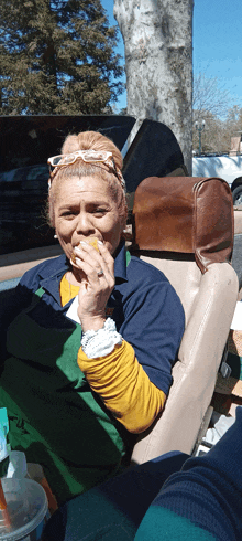 a woman in a green apron is sitting in a car eating a sandwich