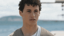 a young man with curly hair is standing in front of a body of water and looking at the camera .