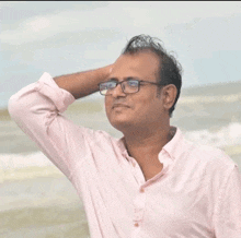 a man with glasses and a pink shirt is standing on the beach