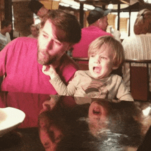 a man in a pink shirt is holding a little boy