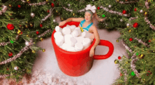 a woman in a bikini is sitting in a cup of hot chocolate surrounded by christmas trees