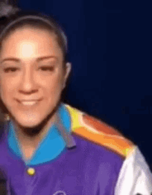 a woman wearing a purple shirt with rainbow stripes on the sleeves is smiling