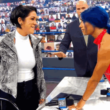 a woman with blue hair is talking to another woman in front of a crowd that is watching a wrestling show